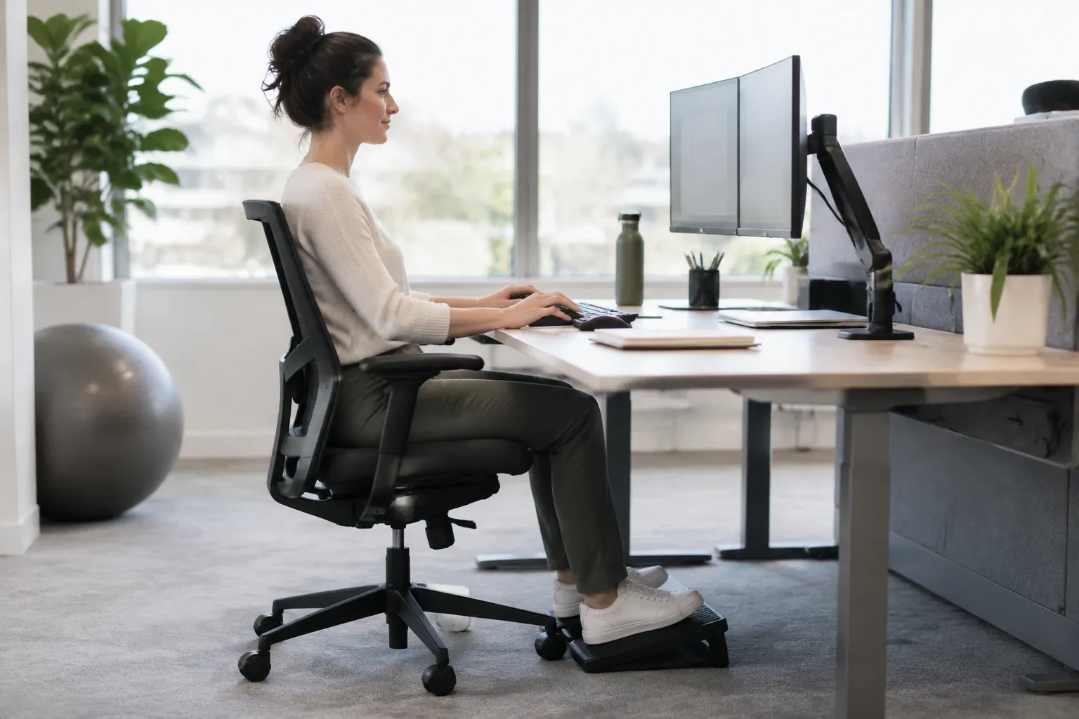 Femme assise droite au bureau, écran double, repose-pieds et chaise ergonomique ajustée